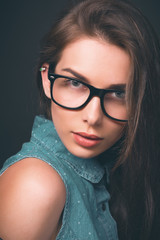 Beautiful young girl. Glasses, denim overalls, a black leather jacket. Sexy girl. Trendy toning image.