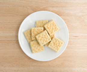 Cream cheese and chives crackers on a white plate atop a wood table.