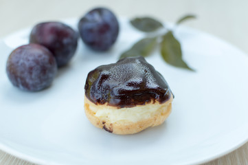 Sweet profiteroles with cream and chocolate glaze and plums on a