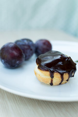 Sweet profiteroles with cream and chocolate glaze and plums on a