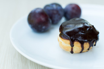 Sweet profiteroles with cream and chocolate glaze and plums on a