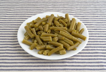 Plate of organic cut green beans on a striped tablecloth side view.