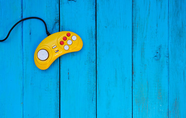 Game controller on a blue wooden background. Yellow joystick. Video game console GamePad. Copy space. 