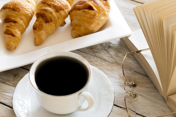 Book and croissants with coffee on the wooden table
