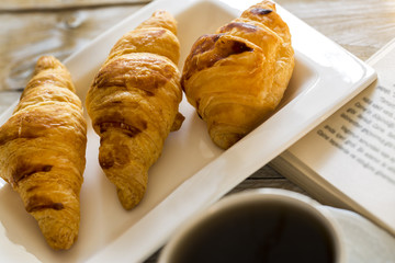 Book and croissants with coffee on the wooden table