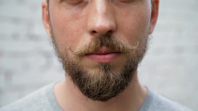 Close up man 's face with a beard and mustache, white brick wall background, zoom out