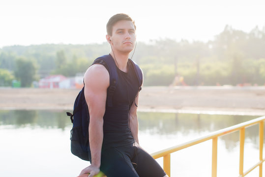 Portrait of athletic man sitting on pier near pond