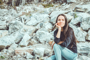 Portrait of young woman in national Highland Park Ruskeala in the Republic of Karelia, Russia. Russian tourism concept. Young brunette female with long hair sitting on big grey stones.