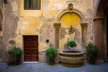 Fototapeta na wymiar un vieux puit avec des plantes en pots dans la cour intérieure jaune d' immeuble Italien de la renaissance