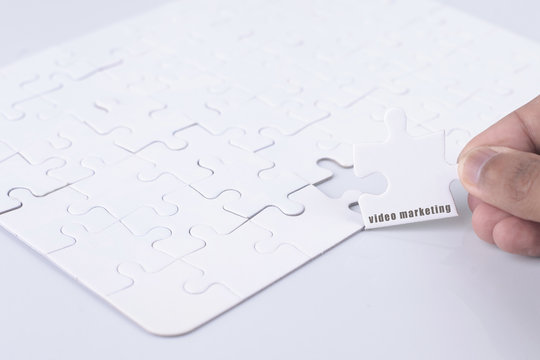 Closeup of businesspeople about to put four puzzle pieces with video marketing