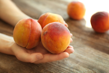 Female hands holding fresh peaches on a wooden background
