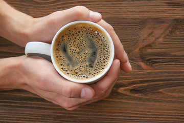 Man hands holding cup of coffee on wooden table