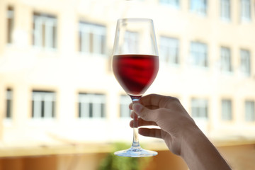 Man hand holding glass of red wine on blurred building background