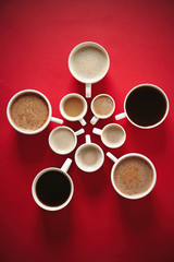 Cups of coffee on red background, top view
