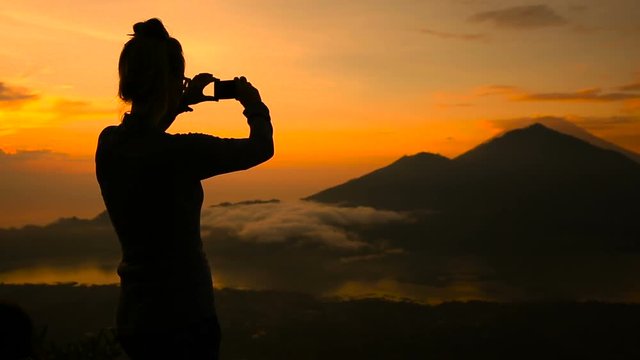 Girl taking pictures of sunrise over Lake Batur, Volcano Agung and Abang, Bali