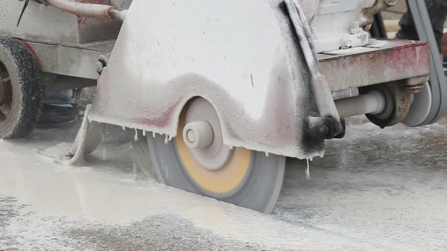 A worker cutting concrete road with diamond saw blade machine