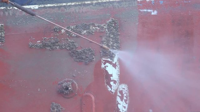 A man working on pressure washer to cleaning boat hull barnacles antifouling and seaweed at the harbor