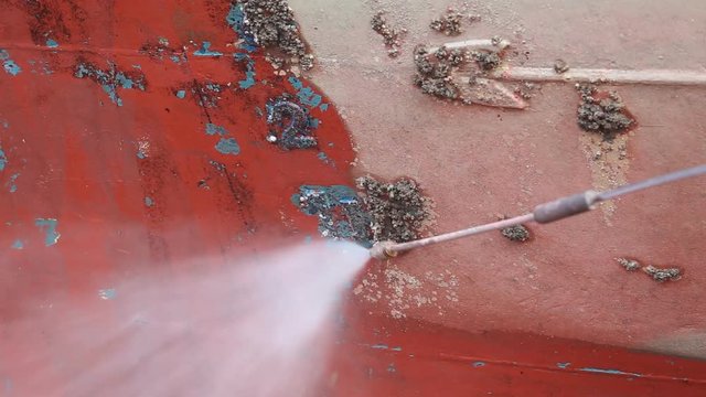 A man working on pressure washer to cleaning boat hull barnacles antifouling and seaweed at the harbor