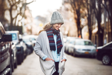 Happy young adult woman walking at beautiful autumn city street wearing colorful scarf and warm hat..