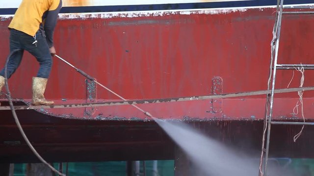 A man working on pressure washer to cleaning boat hull barnacles antifouling and seaweed at the harbor