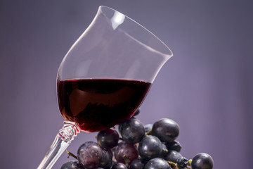 Glass of Rioja red wine beside grapes, on violet