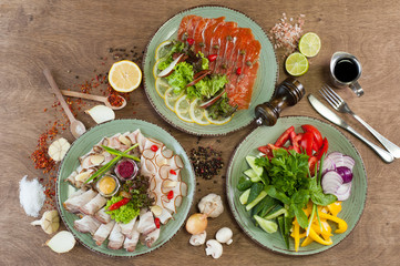 Different vegetables, meat, red fish and other dishes, sauces, snacks and spices on a wooden background