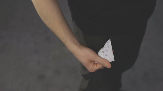 Man's hand crumpling a piece of paper and puts it in the pocket of jeans.