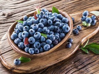 Ripe blueberries in the bowl on the wooden table.