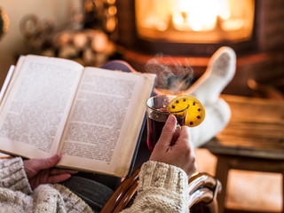 Hot mulled wine and book in woman hands. Relaxing in front of bu