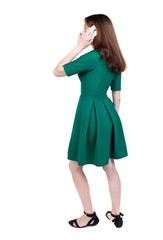 side view of a woman walking with a mobile phone. back view of girl in motion. slender brunette in a green short dress stands sideways and and talking on the phone.