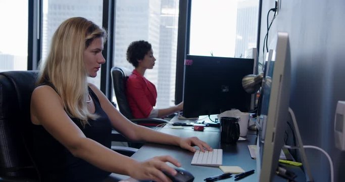 Business women working side by side at computers in creative open-plan city office. Medium shot, recorded hand held in real time.