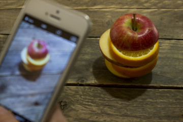 Girl with phone takes a picture of a sliced apple on a wooden ta