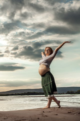 Fototapeta na wymiar Pregnant red haired woman is walking on the river background.