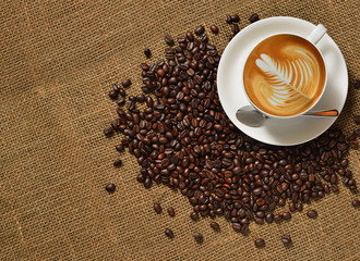 Top view, Cup of coffee latte and coffee beans on burlap background