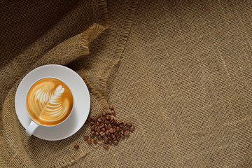Top view of cup of coffee latte and coffee beans on burlap background