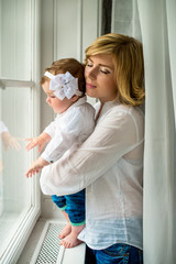 Young mother gently holds the small daughter. Mom and daughter dressed in jeans and white shirt