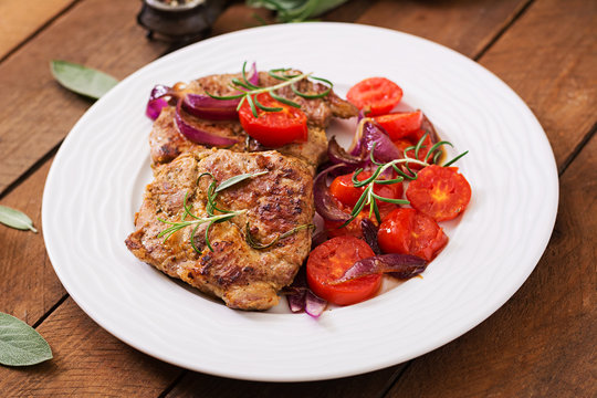 Juicy pork steak with rosemary and tomatoes on a white plate