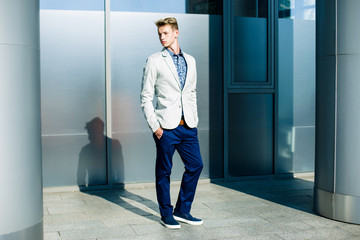 Elegant young handsome man wearing  white jacket and jeans near building