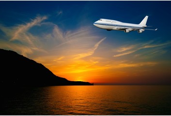 Naklejka na ściany i meble passenger airplane in the clouds at sunset or dawn. Tourist Card. plane on a background of sea and mountains. travel by air transport. flying to the top of the airliner. nobody