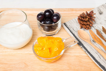 Fresh fruits (orange and grape) with yogurt in a glass bowl on wood tray