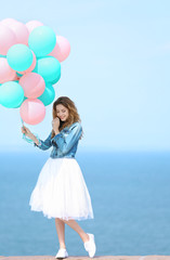 Beautiful young woman with colorful balloons on sea front