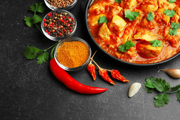 Chicken curry with different spices on dark background