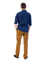 Naklejka premium Back view of man . Standing young guy. man in a blue shirt with the sleeves rolled up, standing with his hands in his pocket.