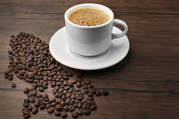 Cup of coffee with beans on wooden background