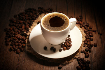 Cup of coffee with beans on wooden background