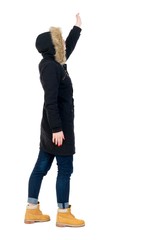 Naklejka premium Back view of beautiful woman welcomes. Girl in warm winter black jacket stands sideways and waving.