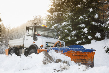 Snow plough making its way through the snowy country road in the morning, clearing it of snow after...