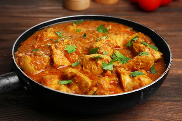 Tasty chicken curry in pan on wooden background