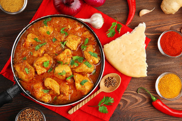 Tasty chicken curry in pan and spices on wooden background