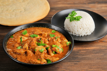 Tasty dinner with chicken curry in bowl on wooden background